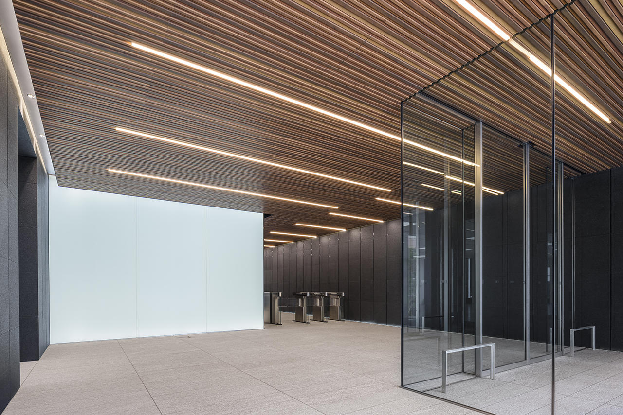ビル全体の照明には、国産木材とLEDライン照明、サインを統合したデザインシステムを採用。エントランスホールでは、天井・壁・床と一体化した線形の光が、来館者をエレベーターホールまで導く