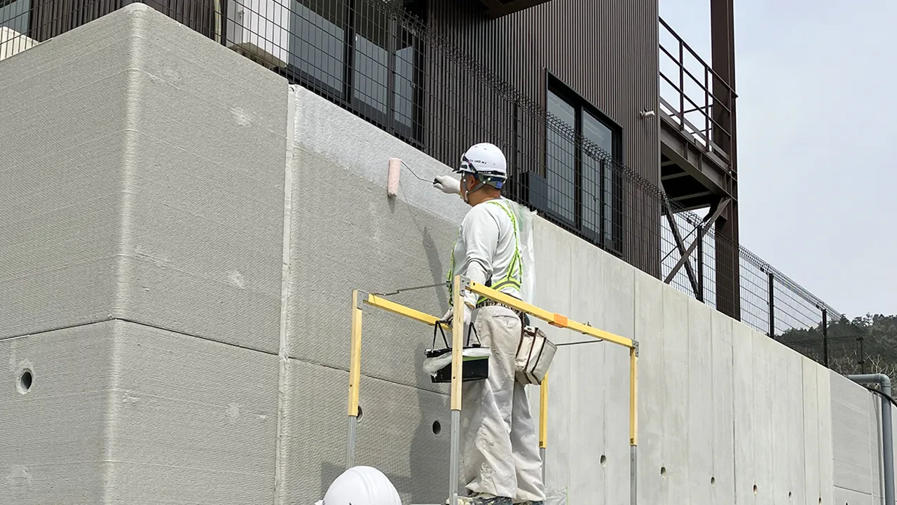 建物外壁のコンクリート擁壁にスキャロップペイントをローラーで塗布する作業員