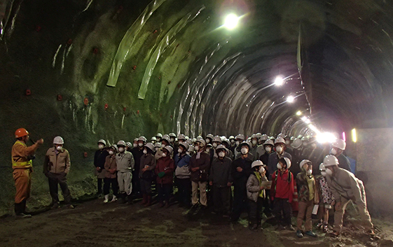 「掘削後は地山が落下しないよう一次掘削完了区間では瞬時にコンクリートを吹き付けます」と説明する大林組職員